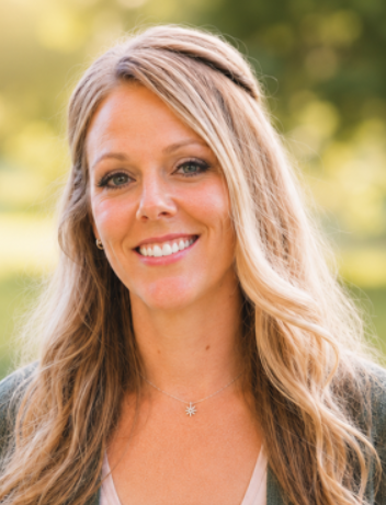 Woman with long blonde hair and a necklace smiles outdoors with blurred greenery in the background, embodying the warmth and tranquility often found in quality therapy services in Ogden, Utah.